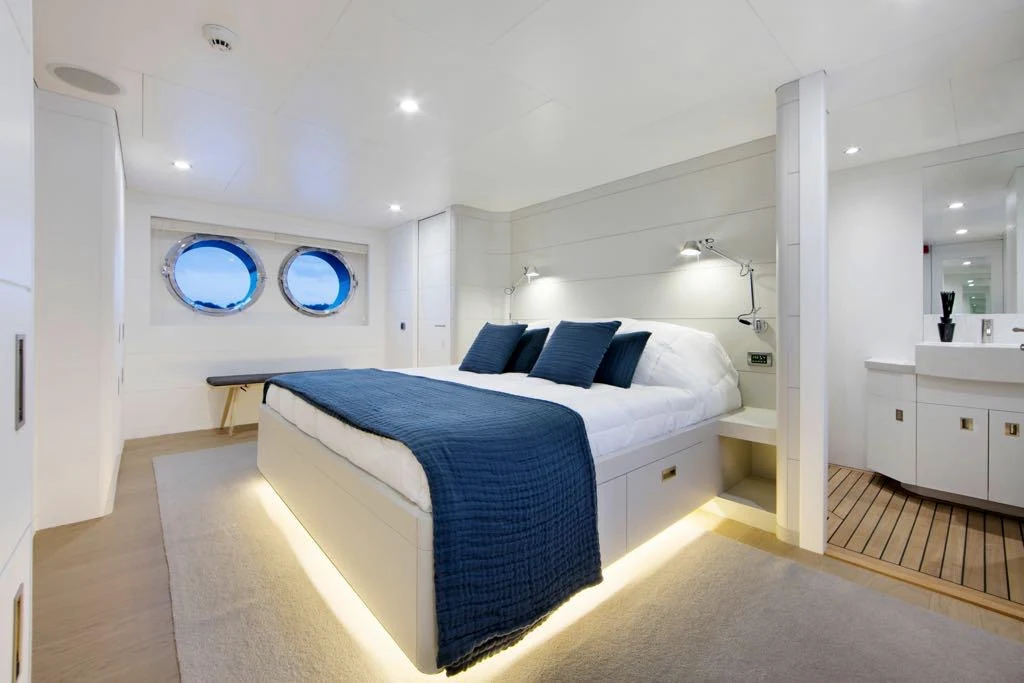Bright private-yacht cabin with navy textiles, round portholes and warm indirect lighting