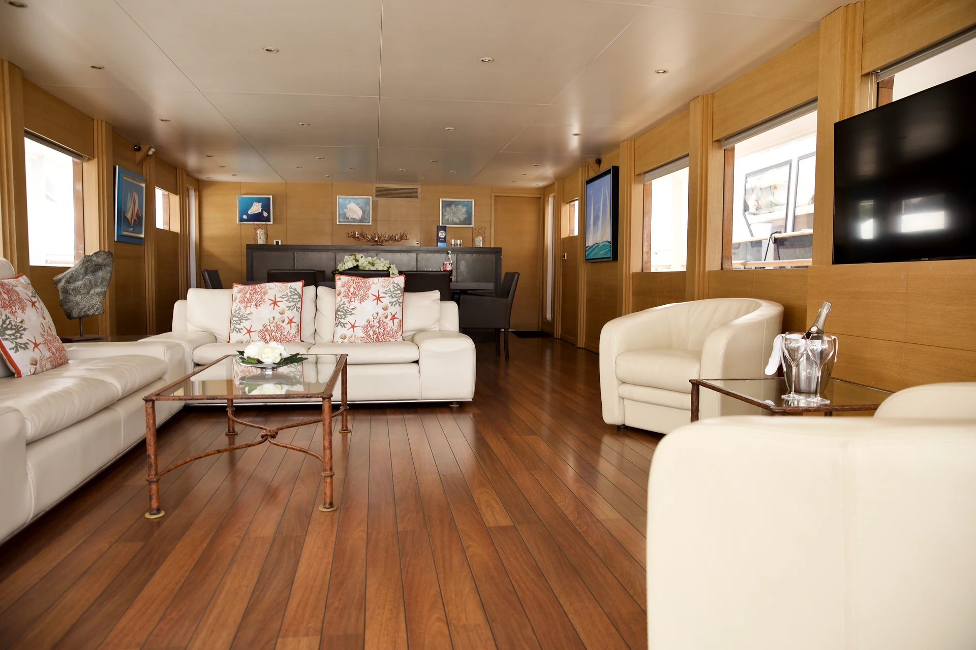 Yacht salon with pale sofas, timber panelling and a glass table