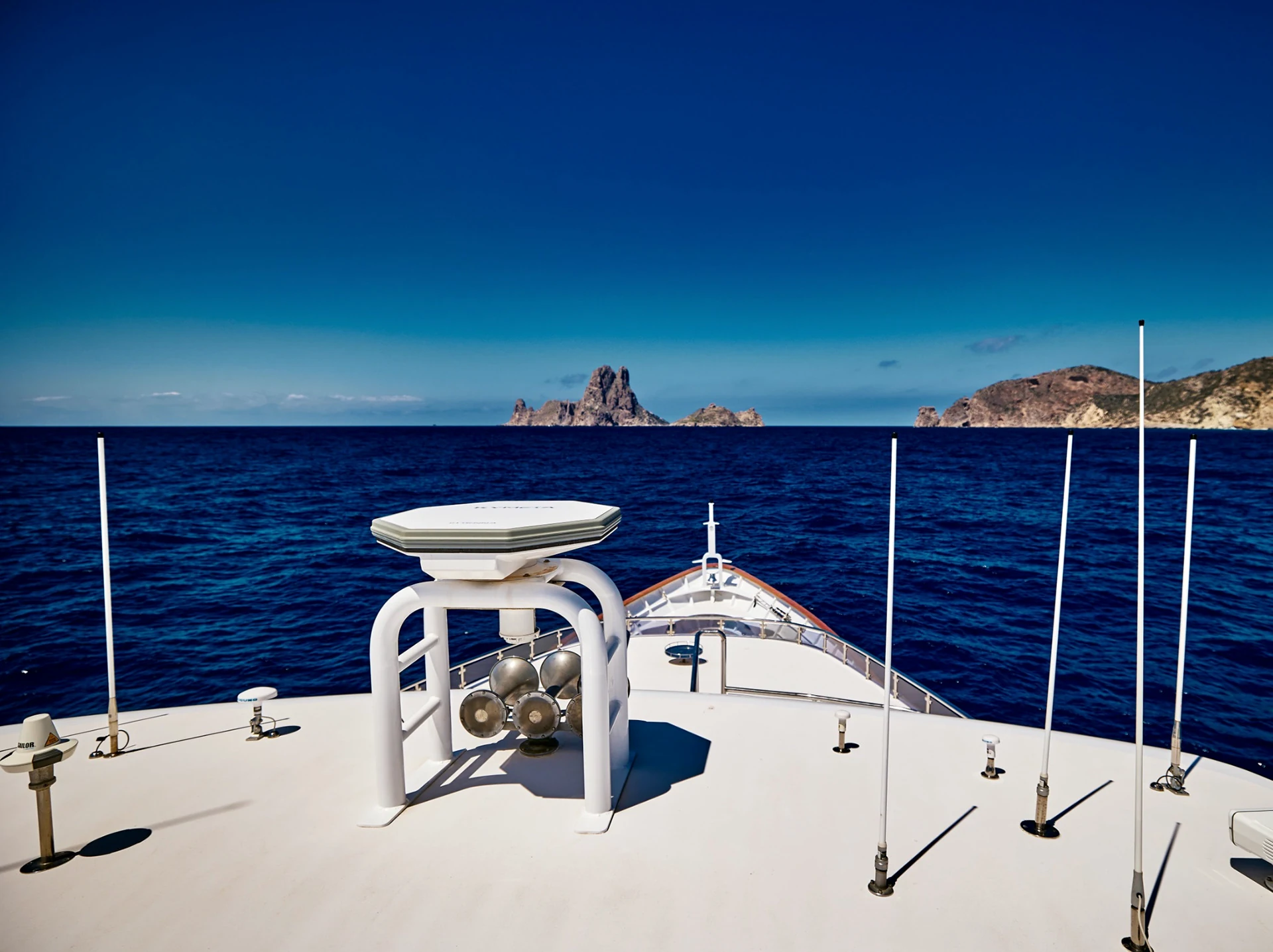 Foredeck view looking across blue water towards a rocky coast